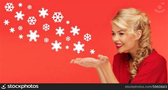 people, holidays, christmas and winter concept - lovely woman in red clothes sending snowflakes from on palms of her hands over red background