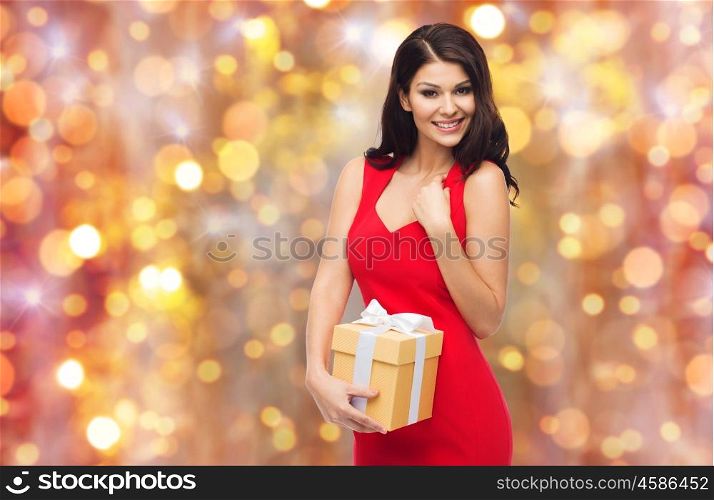people, holidays, christmas, birthday and celebration concept - beautiful sexy woman in red dress with gift box over lights background