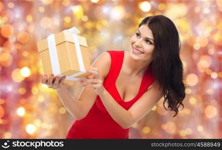 people, holidays, christmas, birthday and celebration concept - beautiful sexy woman in red dress with gift box over lights background