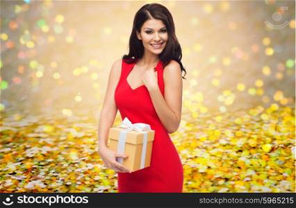 people, holidays, christmas, birthday and celebration concept - beautiful sexy woman in red dress with gift box over golden glitter or lights background