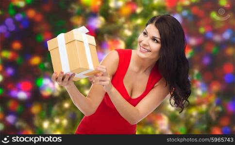 people, holidays, christmas, birthday and celebration concept - beautiful sexy woman in red dress with gift box over holidays lights background