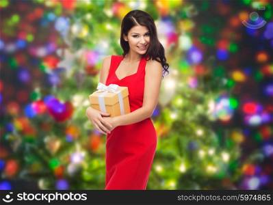 people, holidays, christmas, birthday and celebration concept - beautiful sexy woman in red dress with gift box over party lights background