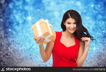 people, holidays, christmas, birthday and celebration concept - beautiful sexy woman in red dress with gift box over blue glitter and lights background