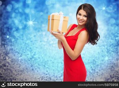 people, holidays, christmas, birthday and celebration concept - beautiful sexy woman in red dress with gift box over blue glitter and lights background