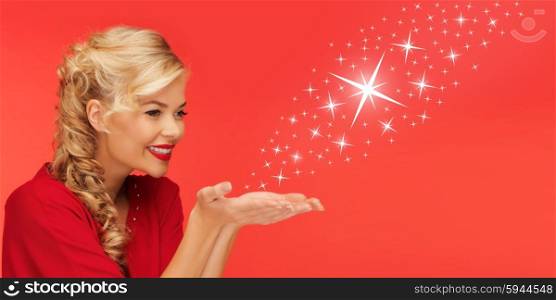 people, holidays, christmas, magic and winter concept - lovely woman in red clothes sending stars from on palms of her hands over red background