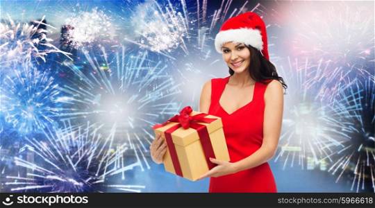 people, holidays, christmas, new year party and celebration concept - beautiful sexy woman in red dress and santa hat with gift box over night city and firework background