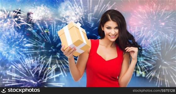 people, holidays, christmas, new year party and celebration concept - beautiful sexy woman in red dress with gift box over night city and firework background