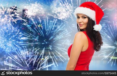 people, holidays, christmas, new year party and celebration concept - beautiful sexy woman in santa hat and red dress over night city and firework background