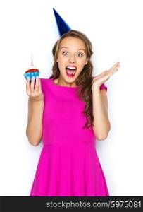 people, holidays, emotion, expression and celebration concept - happy young woman or teen girl in pink dress and party cap with birthday cupcake