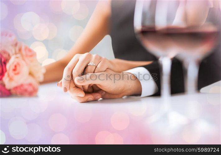 people, holidays, engagement and love concept - engaged couple holding hands with diamond ring over holidays lights background