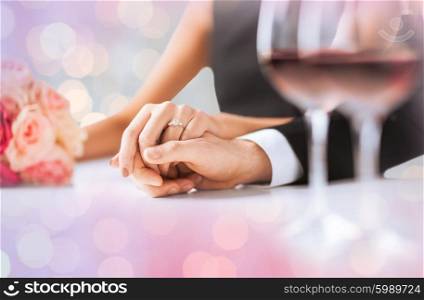 people, holidays, engagement and love concept - engaged couple holding hands with diamond ring over holidays lights background