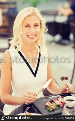 people, holidays, food and leisure concept - happy woman with fork and knife eating squid for dinner at restaurant terrace