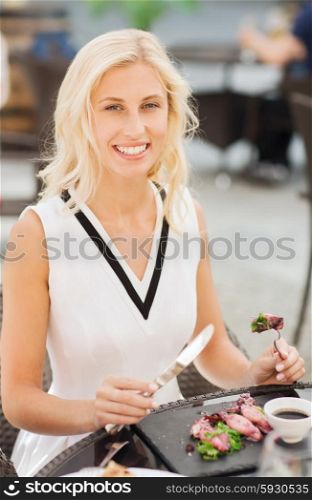 people, holidays, food and leisure concept - happy woman with fork and knife eating squid for dinner at restaurant terrace
