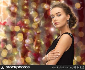 people, holidays, jewelry and glamour concept - beautiful woman wearing earrings over christmas lights background