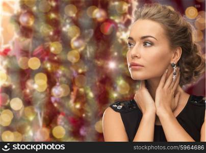 people, holidays, jewelry and glamour concept - beautiful woman wearing earrings over christmas lights background