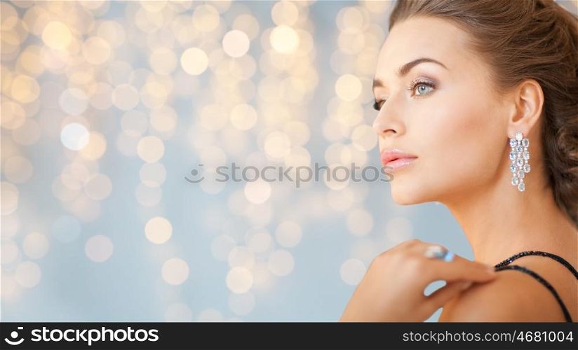 people, holidays, jewelry and luxury concept - close up of woman in evening dress with diamond earring over lights background