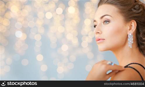 people, holidays, jewelry and luxury concept - close up of woman in evening dress with diamond earring over lights background