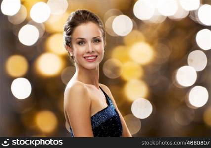 people, holidays, jewelry and luxury concept - smiling woman in evening dress and pearl earring over lights background