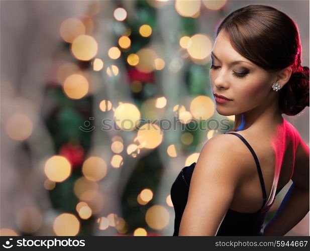 people, holidays, jewelry and luxury concept - woman face with diamond earring over christmas tree lights background