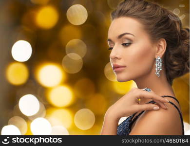 people, holidays, jewelry and luxury concept - woman in evening dress and diamond earring over lights background