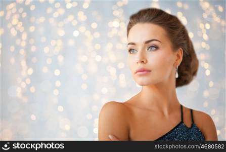 people, holidays, jewelry and luxury concept - woman in evening dress and diamond earring over lights background