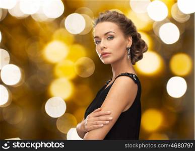 people, holidays, jewelry and luxury concept - woman in evening dress and earring over lights background