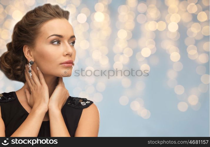 people, holidays, jewelry and luxury concept - woman in evening dress and earring over lights background