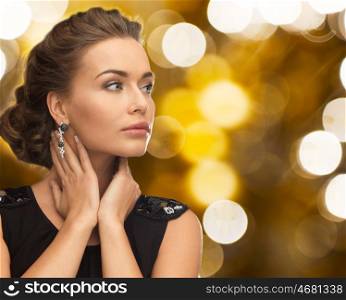 people, holidays, jewelry and luxury concept - woman in evening dress and earring over lights background