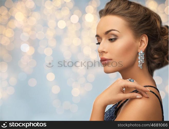 people, holidays, jewelry and luxury concept - woman in evening dress with diamond earring over lights background