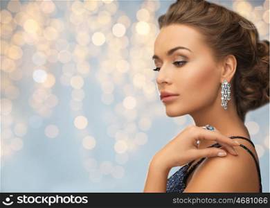 people, holidays, jewelry and luxury concept - woman in evening dress with diamond earring over lights background