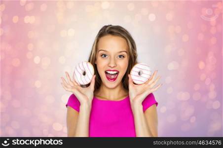 people, holidays, junk food and fast food concept - happy young woman or teen girl in pink dress with donuts over rose quartz and serenity lights background