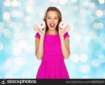 people, holidays, junk food and fast food concept - happy young woman or teen girl in pink dress with donuts over blue holidays lights background