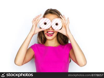 people, holidays, junk food and fast food concept - happy young woman or teen girl in pink dress having fun, looking through donuts and showing tongue