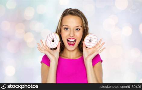 people, holidays, junk food and fast food concept - happy young woman or teen girl in pink dress with donuts over holidays lights background