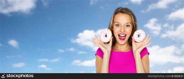 people, holidays, junk food and fast food concept - happy young woman or teen girl in pink dress with donuts over blue sky and clouds background