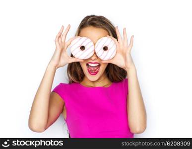 people, holidays, junk food and fast food concept - happy young woman or teen girl in pink dress having fun and looking through donuts