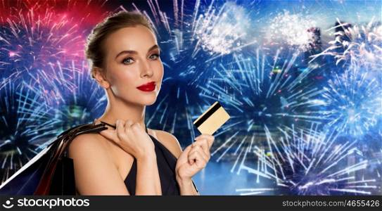 people, holidays, luxury and sale concept - beautiful woman with credit card and shopping bags over night city firework background