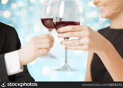 people, holidays, marriage and celebration concept - happy engaged couple clinking wine glasses over blue holidays lights background