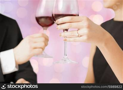 people, holidays, marriage and celebration concept - happy engaged couple clinking wine glasses over holidays lights background