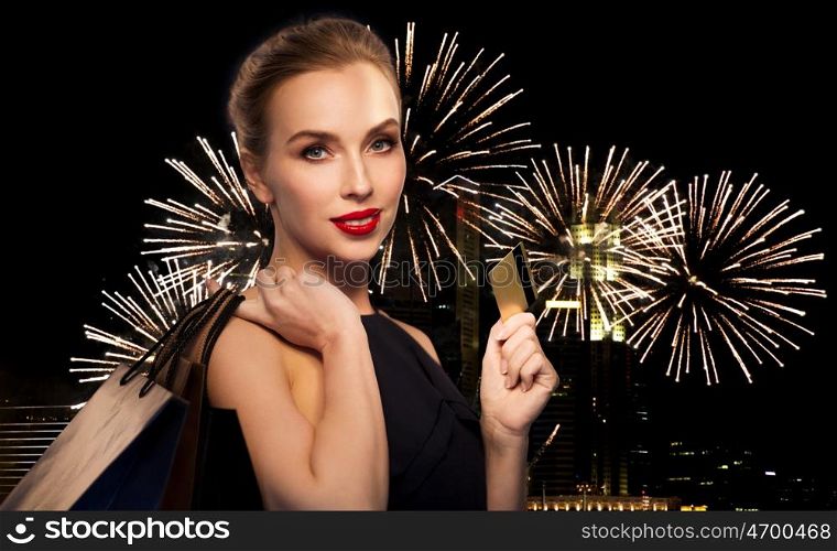 people, holidays, new year, luxury and sale concept - beautiful woman with credit card and shopping bags over night city firework lights background