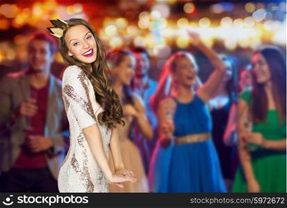 people, holidays, nightlife and celebration concept - happy young woman or teen girl in party dress and princess crown at night club party over crowd and lights background