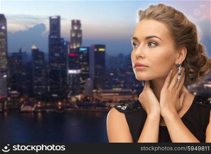 people, holidays, nightlife and glamour concept - beautiful woman wearing earrings over evening singapore city background