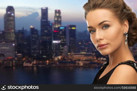 people, holidays, nightlife and glamour concept - beautiful woman wearing earrings over evening singapore city background