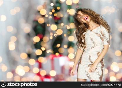 people, holidays, party and fashion concept - happy young woman or teen girl in fancy dress with sequins and long wavy hair dancing over christmas tree lights background