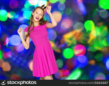 people, holidays, party and fashion concept - happy young woman or teen girl in pink dress and princess crown dancing over disco lights background