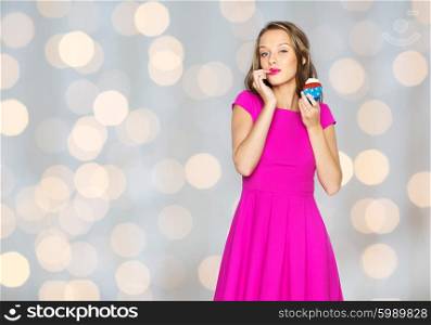 people, holidays, party, junk food and celebration concept - happy young woman or teen girl in pink dress with birthday cupcake over lights background