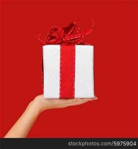 people, holidays, present, surprise and birthday concept - close up hand holding christmas gift box over red background