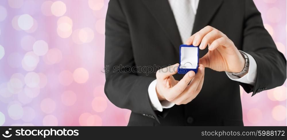 people, holidays, presents and proposal concept - close up of man with gift box and engagement ring over holidays lights background