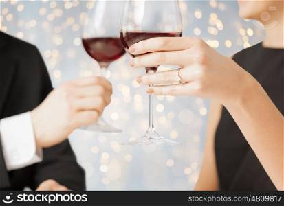 people, holidays, proposal, engagement and celebration concept - close up of engaged couple hands with ring and red wine glasses over lights background