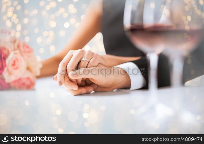 people, holidays, proposal, engagement and wedding concept - close up of engaged couple holding hands over lights background